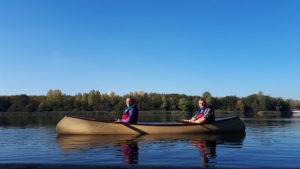 Zu zweit paddeln im Kanadier auf dem Otto-Maigler-See. Der blaue Himmel spiegelt sich im See.