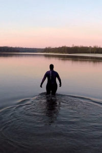 Janine geht im Sonnenaufgang im Neoprenanzug ins Wasser